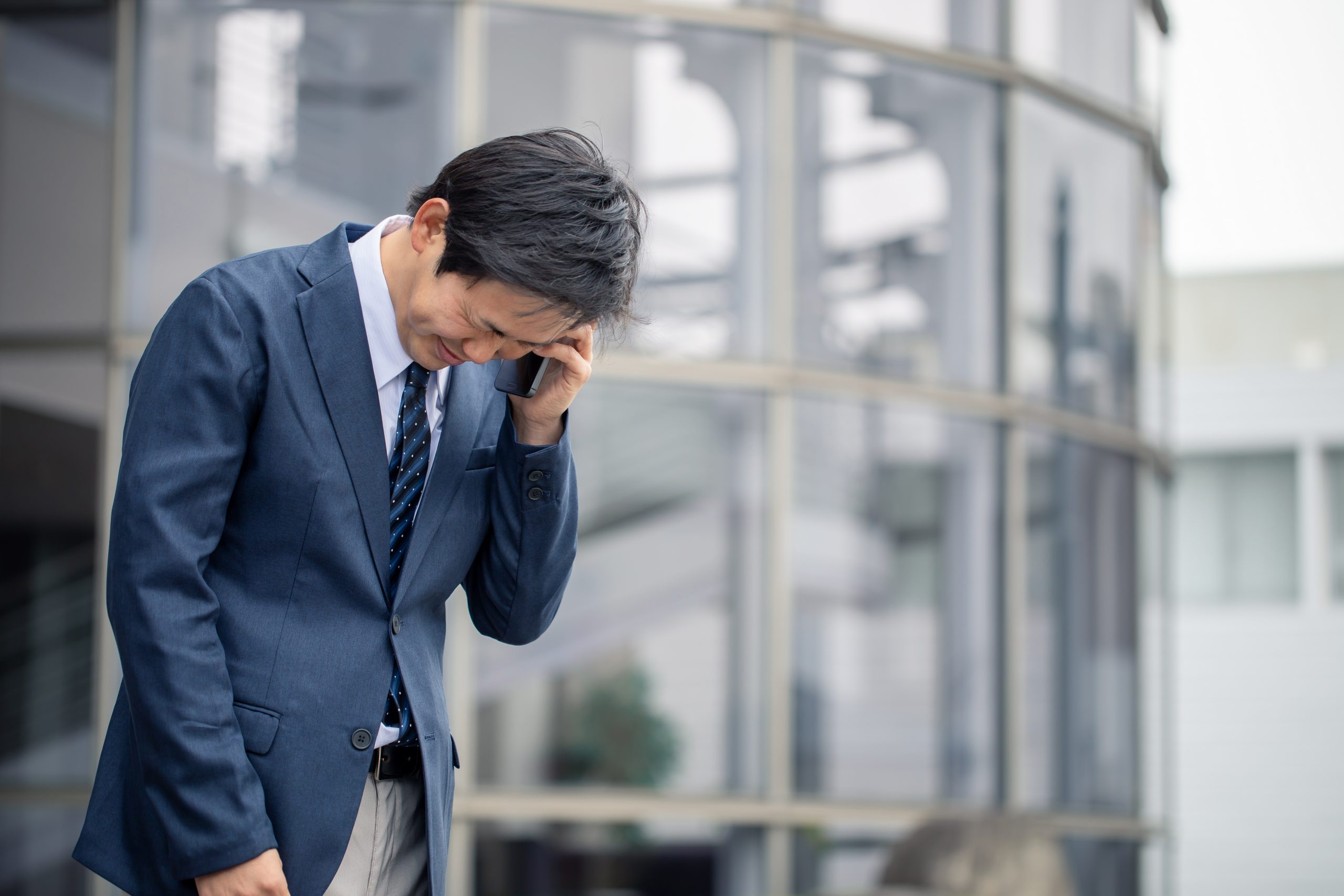 Japanese man in a suit apologizing over a phone